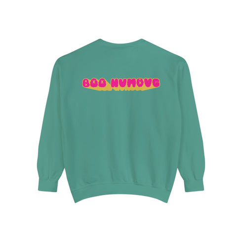 A holiday sweatshirt featuring a cute ghost character wearing a Santa hat, with two smaller ghosts on either side. Above them is the playful text "Boo Humbug," surrounded by snowflakes and festive elements. The design humorously combines spooky and festive themes for a unique holiday look.